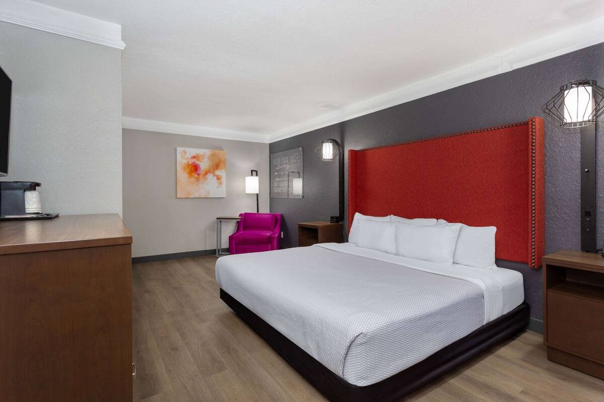 Une chambre d’hôtel avec un grand lit, un bureau, une chaise et un mur d’accent rouge.