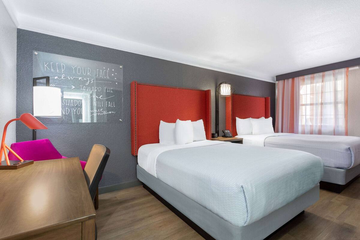 Une chambre d’hôtel avec deux lits, un bureau, une chaise, une lampe et un tableau noir sur lequel sont écrites des citations inspirantes.