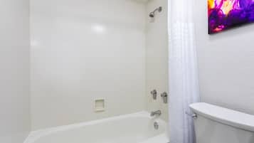 A bathroom with a white bathtub, a showerhead, and a toilet.