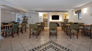 A dining area with multiple tables and chairs, a flat-screen TV mounted on the wall, and a patterned rug on the floor.