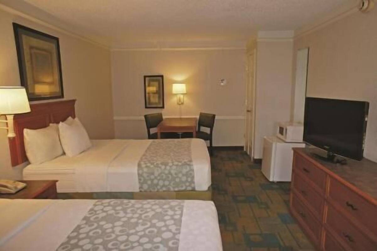 Une chambre d’hôtel avec deux lits, un bureau, une chaise, une télévision et une commode.