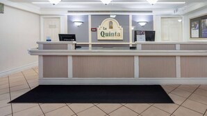 A reception area with a counter, a sign reading "La Quinta," and a black doormat.