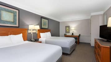 A hotel room with two beds, a desk, a chair, a television, and framed artwork on the walls.