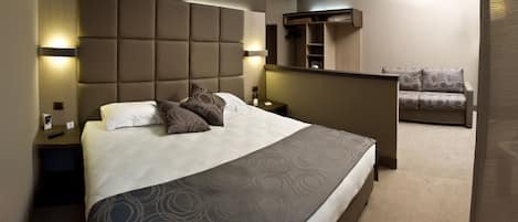 Habitación de hotel con una cama grande, una mesita de noche, un armario empotrado y una zona de estar con sofá.