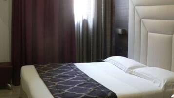 Ein Hotelzimmer mit einem groĂen Bett, einem Kopfteil, einem Nachttisch und einem Fenster mit VorhĂ€ngen.