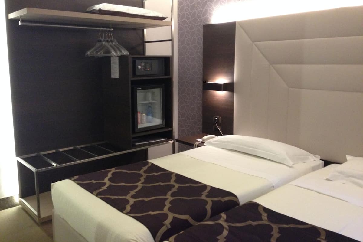 A hotel room with a bed, a minibar, a refrigerator, and a built-in wardrobe.