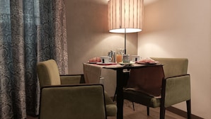 Un comedor con una mesa dispuesta para dos personas, que incluye una lámpara, platos, tazas y una cafetera.