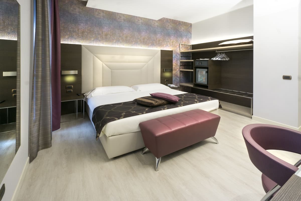 A modern hotel room with a large bed, a seating area, and a television.