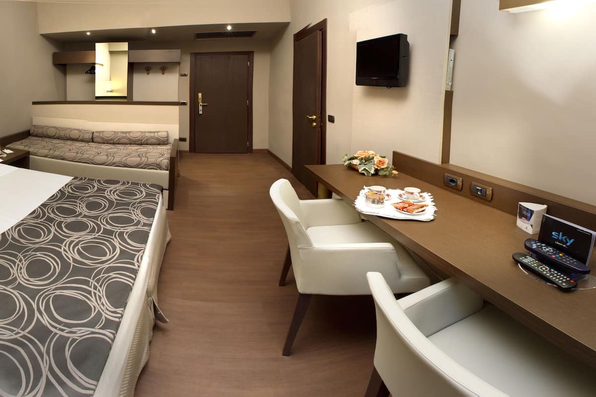 A hotel room with a bed, a sofa bed, a desk with a TV, and a chair.