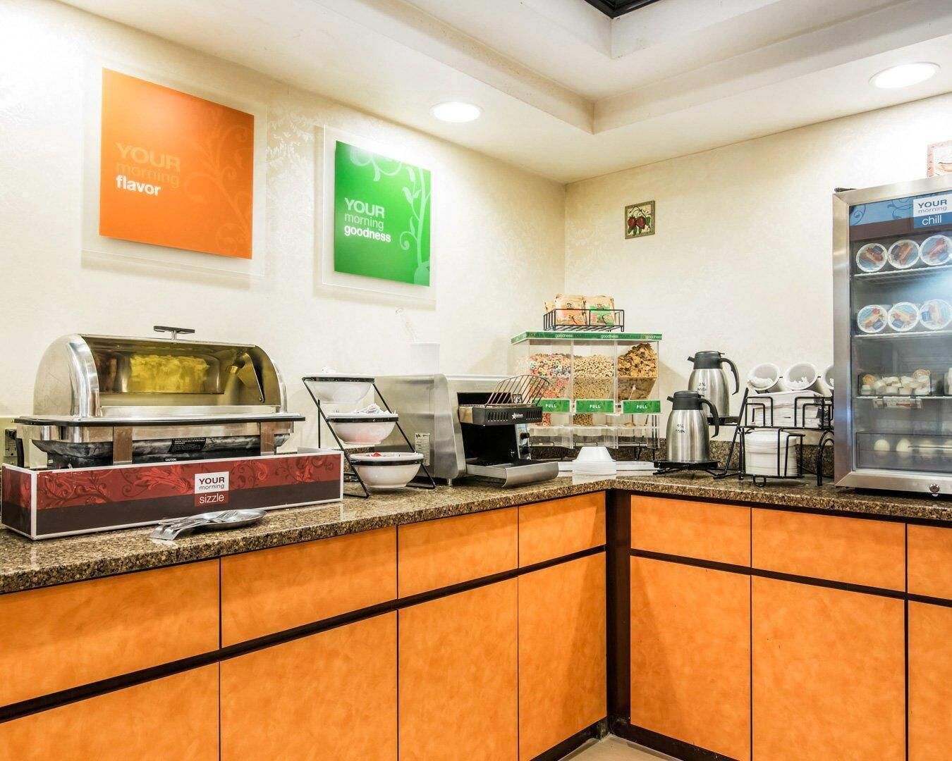 A breakfast bar with a sizzle station, coffee makers, and a refrigerated display.