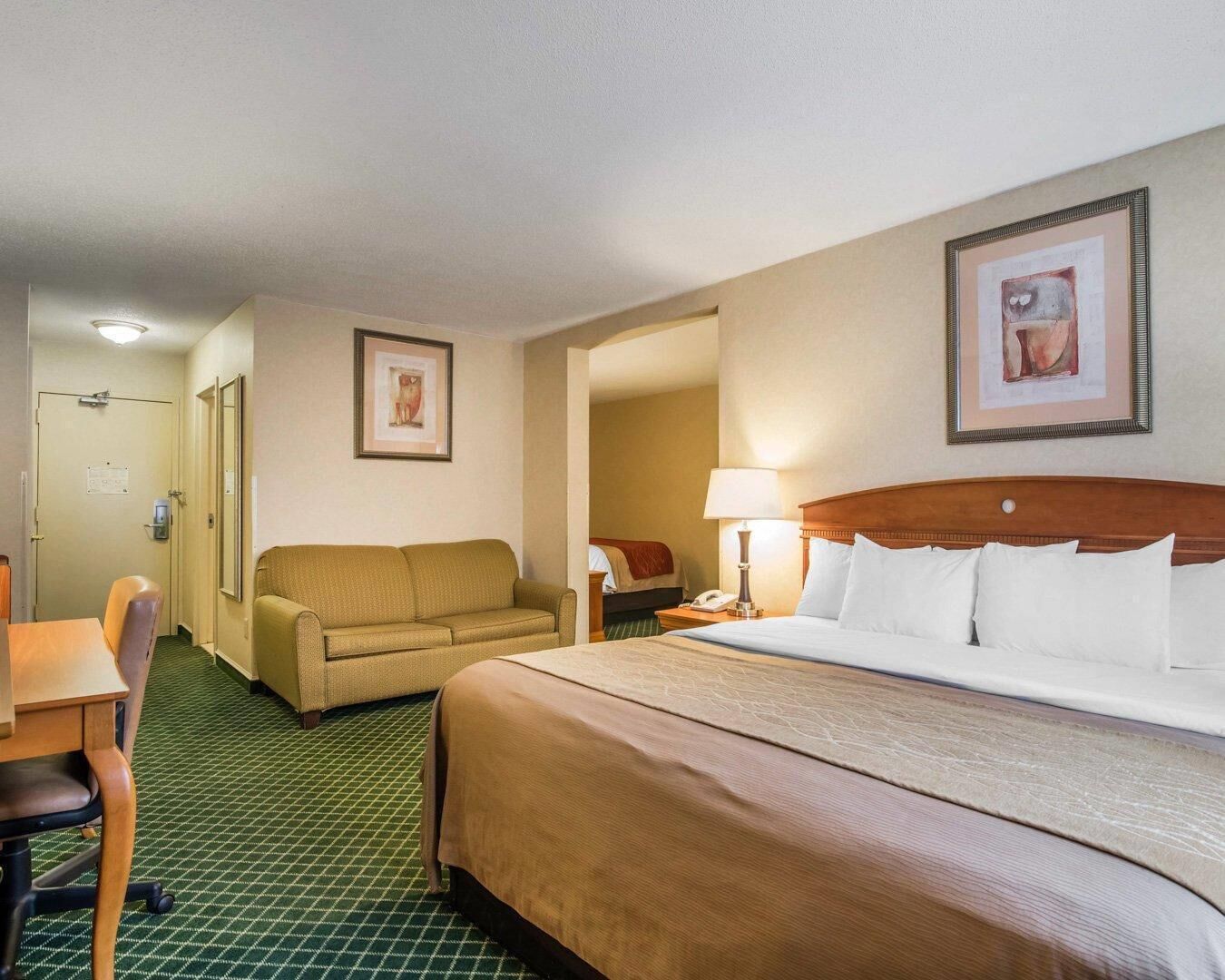 A hotel room with a bed, a sofa, a desk, and a chair.