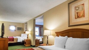 Une chambre d’hôtel avec un grand lit, une télévision, un bureau avec un ordinateur et une salle de bain visible à travers une porte ouverte.
