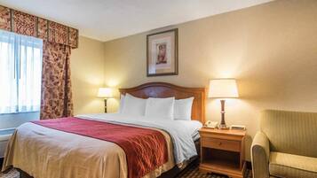A hotel room with a bed, two bedside lamps, a chair, a framed picture on the wall, and a patterned carpet.