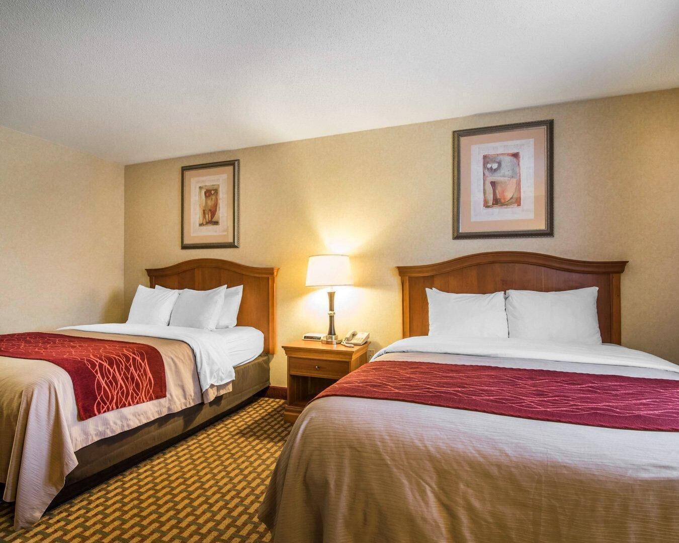 A hotel room with two beds, a nightstand with a lamp, and framed artwork on the walls.