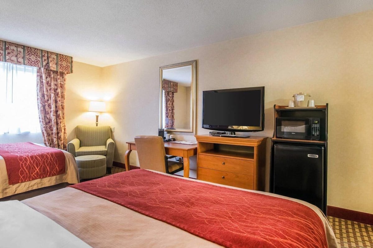 A hotel room with two beds, a television, a desk with a chair, a microwave, and a refrigerator.
