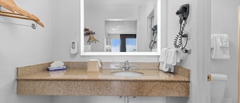 A bathroom with a granite countertop sink, a mirror, a hairdryer, and a towel rack.