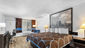 Ein Hotelzimmer mit einem großen Bett, einem Schreibtisch, einem Sessel, einem Fenster mit Vorhängen und einem Stadtbild an der Wand.
