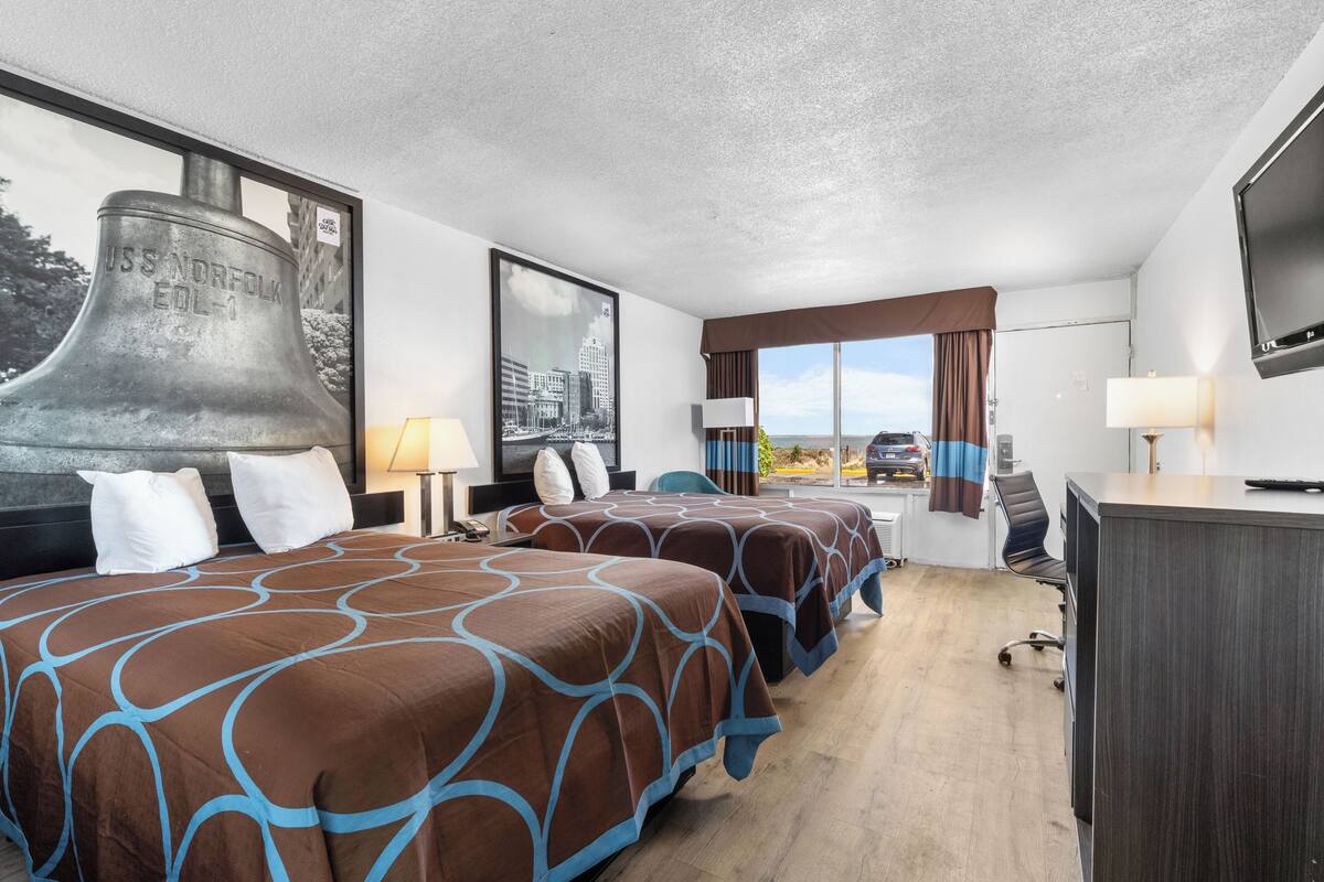 Une chambre d’hôtel avec deux lits, un bureau, une télévision et une grande fenêtre donnant sur un beau paysage.