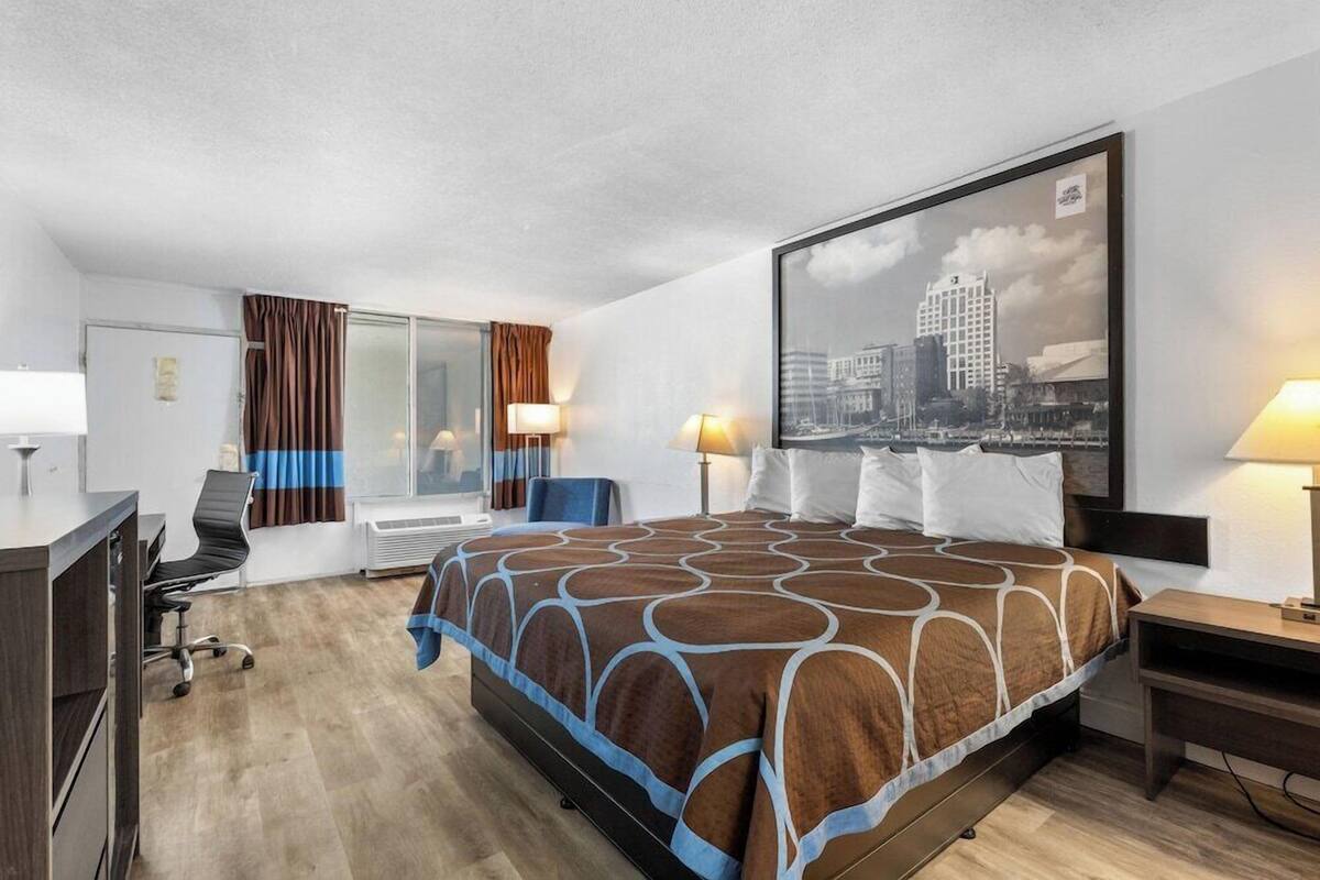 Een hotelkamer met een bed, bureau, stoel en een stadslandschap op de muur.