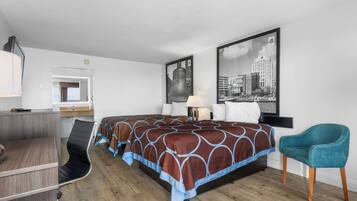 A hotel room with a bed, desk, chair, and two framed pictures on the wall.