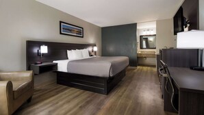 Una habitación de hotel con cama, mesita de noche, lámpara, silla y televisor.