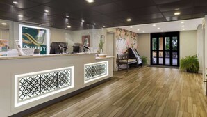 Un área de recepción con diseño moderno, que incluye un mostrador de recepción, un cartel grande que dice 'QUALITY' y una pantalla decorativa con un diseño geométrico.