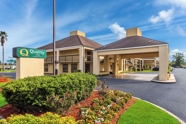 A Quality Inn by Choice Hotels with a covered entrance, landscaped garden, and a clear blue sky.