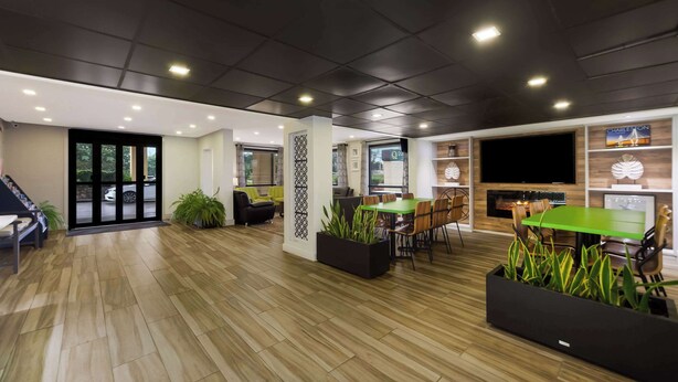 Un espacio interior amplio con suelo de madera, una zona de estar con una mesa verde y un televisor de pantalla plana grande montado en la pared.
