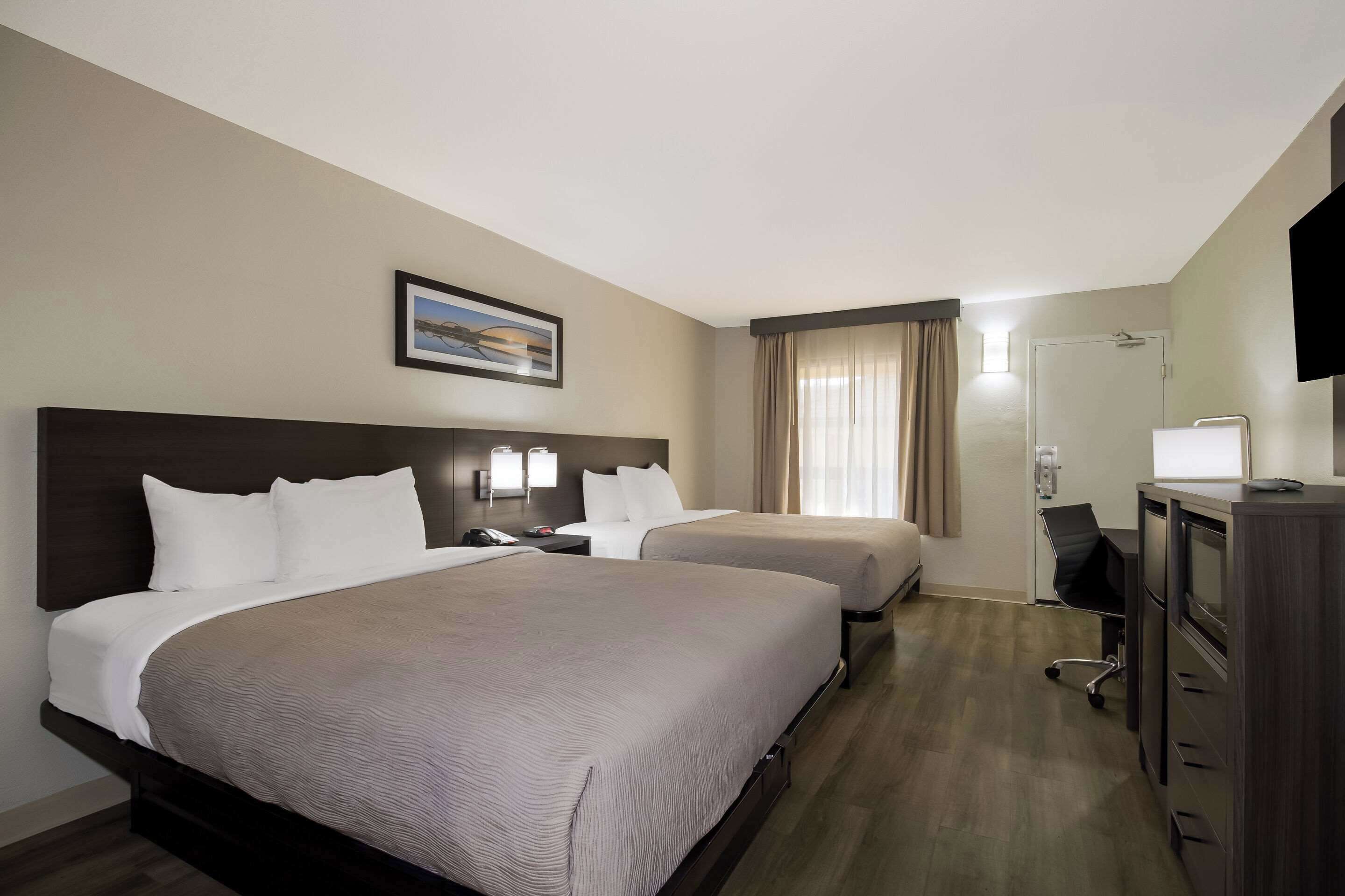 A hotel room with two beds, a desk, a chair, a TV, and a bathroom door.