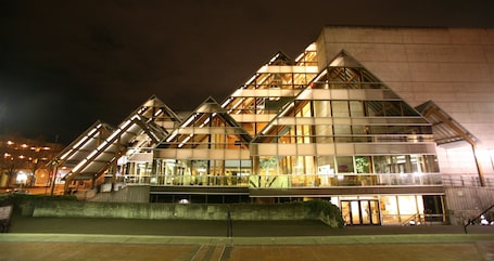 A modern building with a glass facade and multiple levels, featuring a prominent entrance and a staircase leading to the upper levels.
