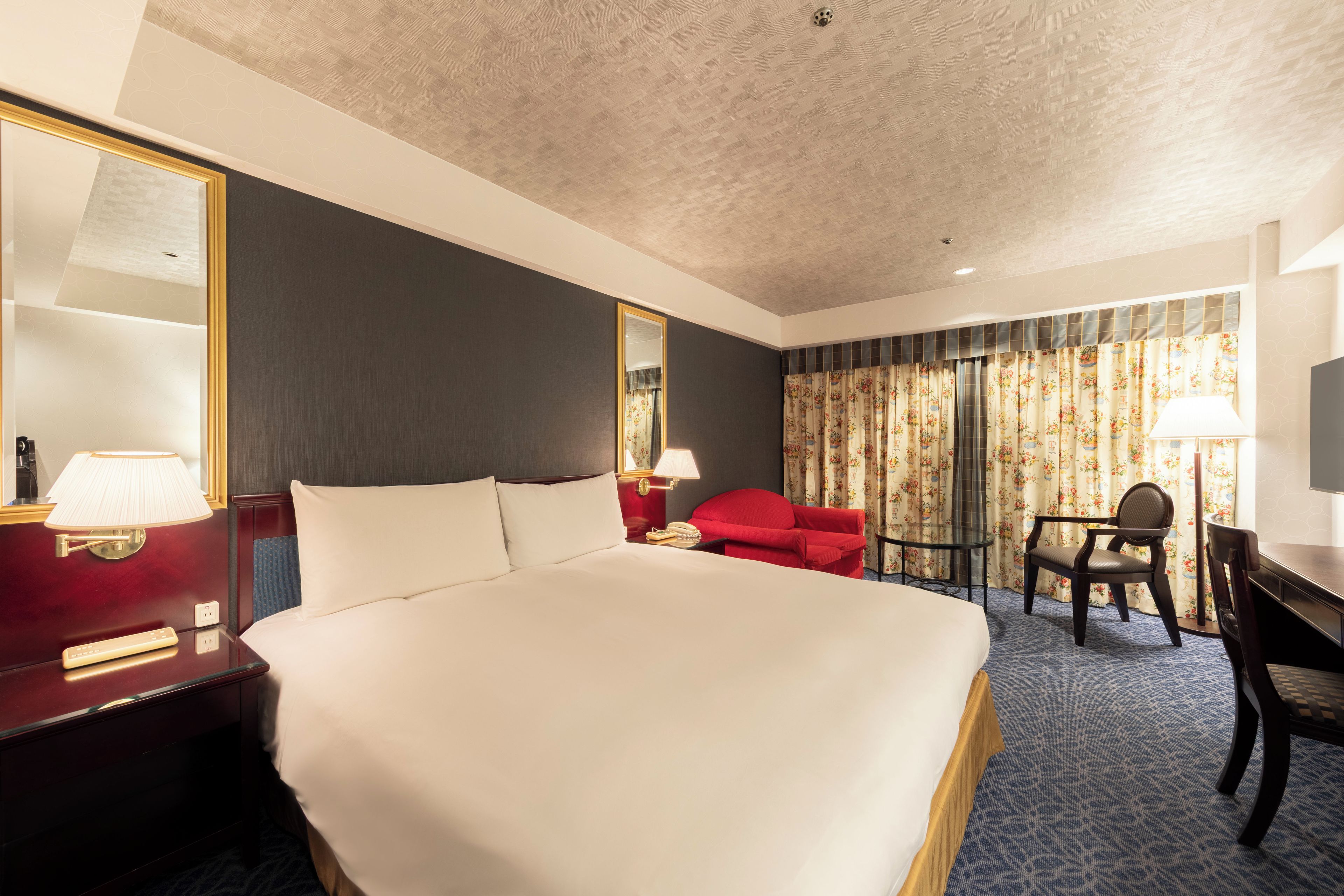 Une chambre d’hôtel avec un grand lit, un bureau, une chaise, une télévision et une fenêtre avec des rideaux.