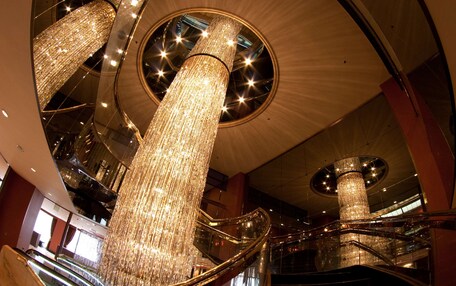 A grand atrium with multiple escalators, large chandeliers, and reflective surfaces.