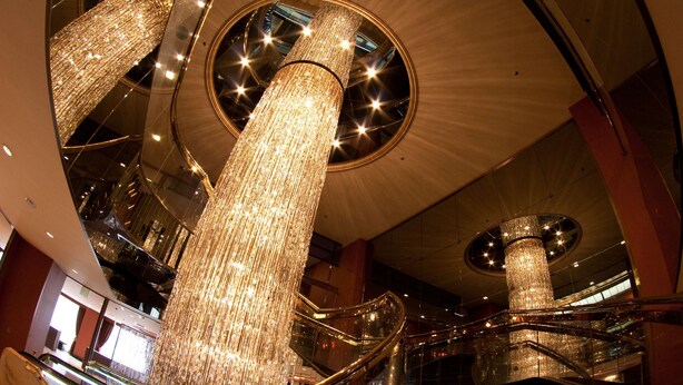 A grand atrium with multiple escalators, large chandeliers, and reflective surfaces.