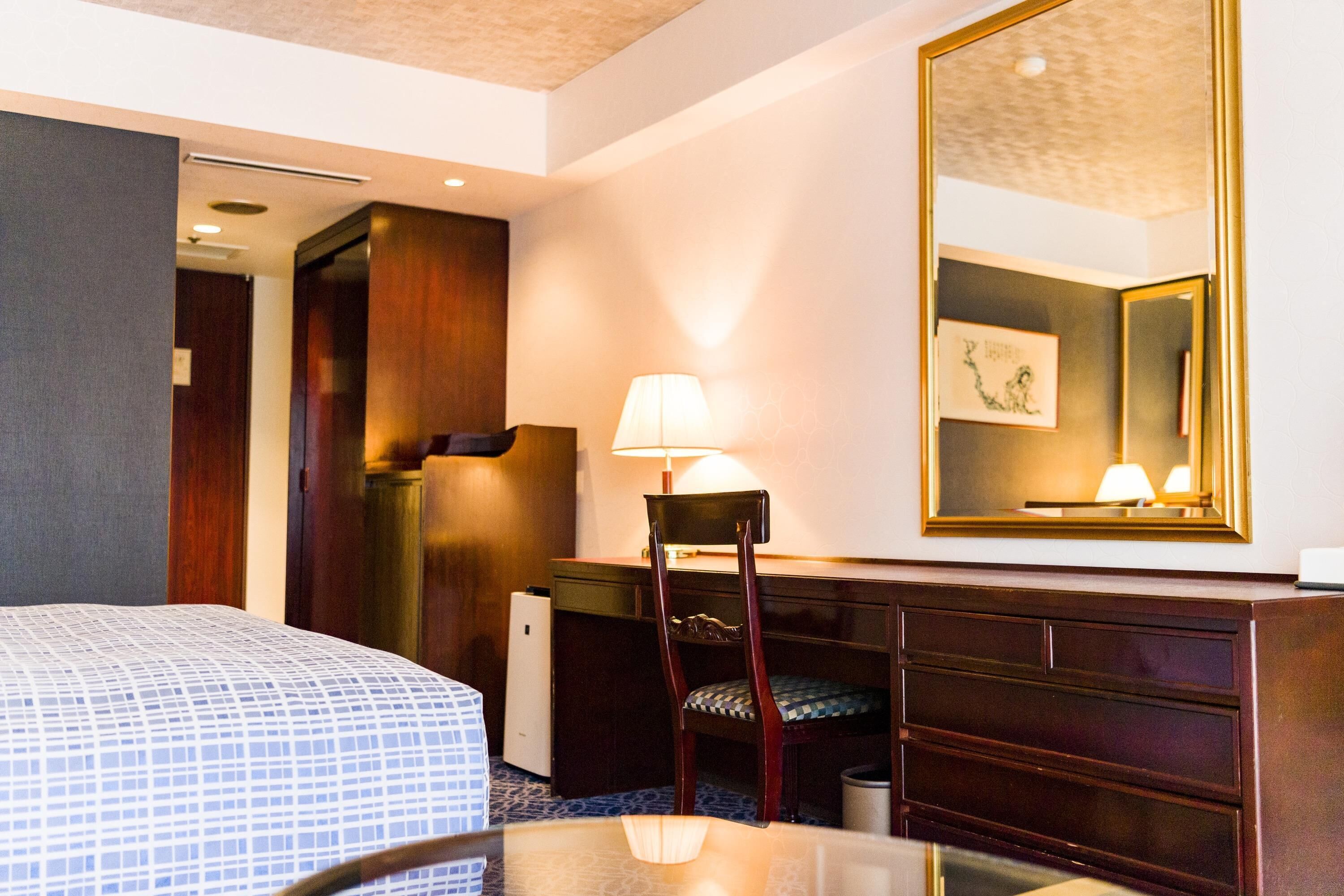 Ein Hotelzimmer mit Bett, Schreibtisch, Stuhl, Kommode, Spiegel und Lampe.