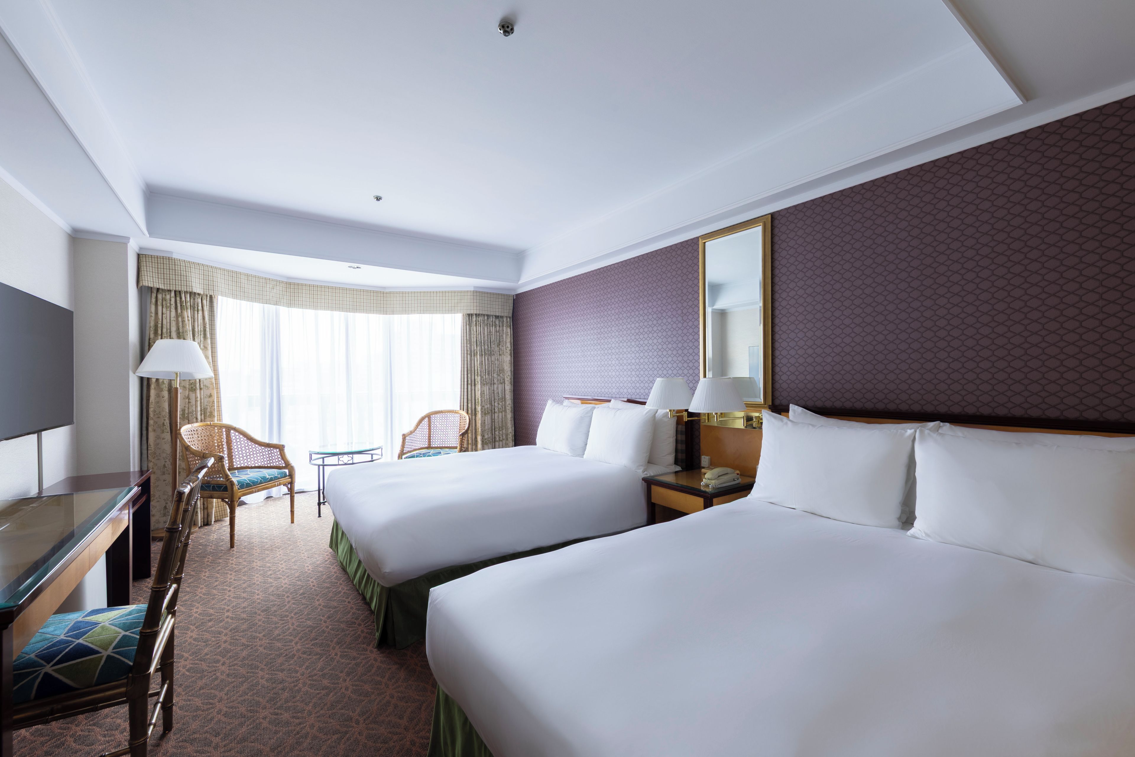 A hotel room with two beds, a desk, a chair, a lamp, and a large mirror.