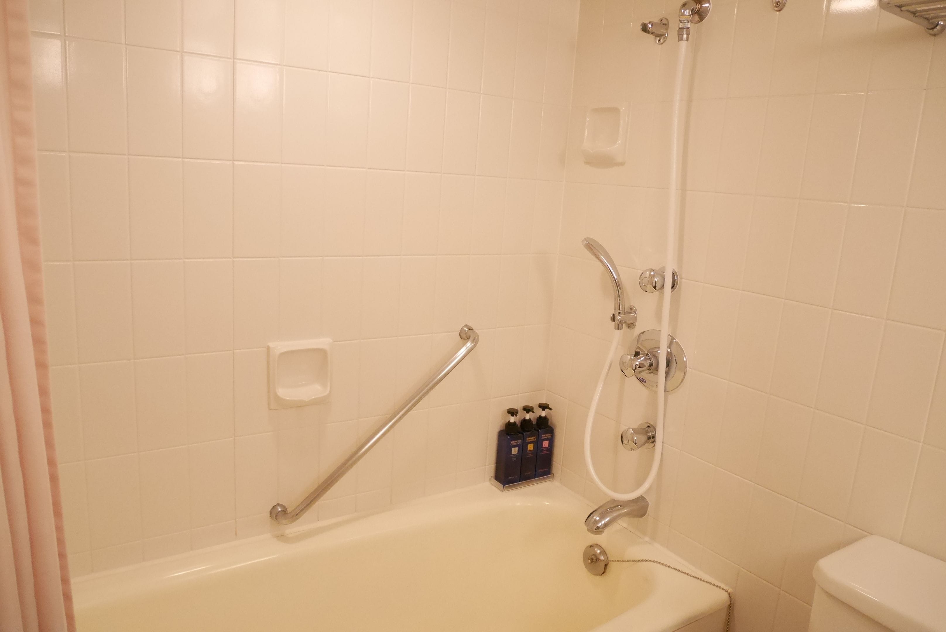 A bathroom with a bathtub, a shower, and a toilet. There are hand soap dispensers and a grab bar installed.