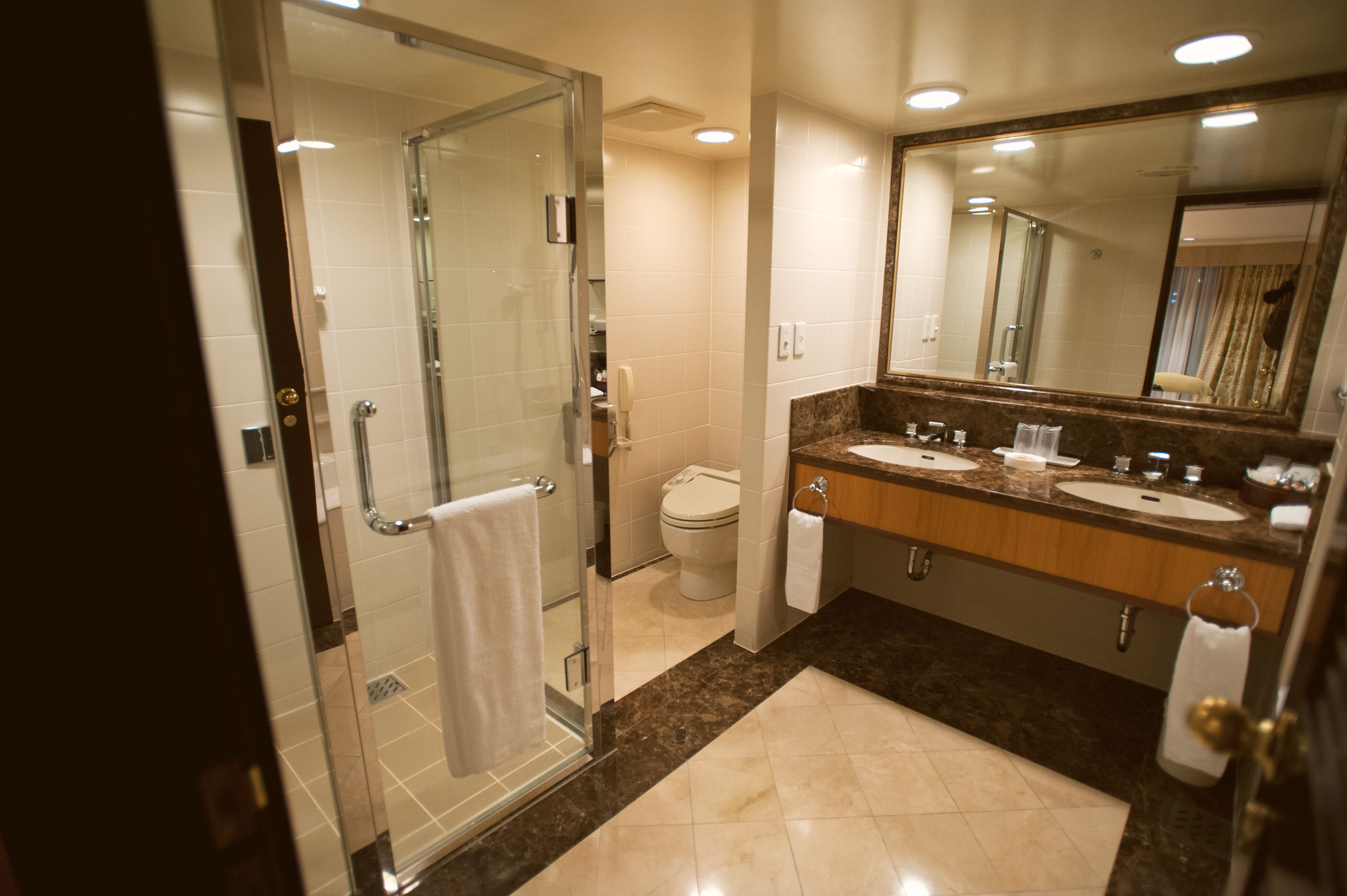 A modern bathroom with a glass-enclosed shower, two sinks, a large mirror, and a toilet.