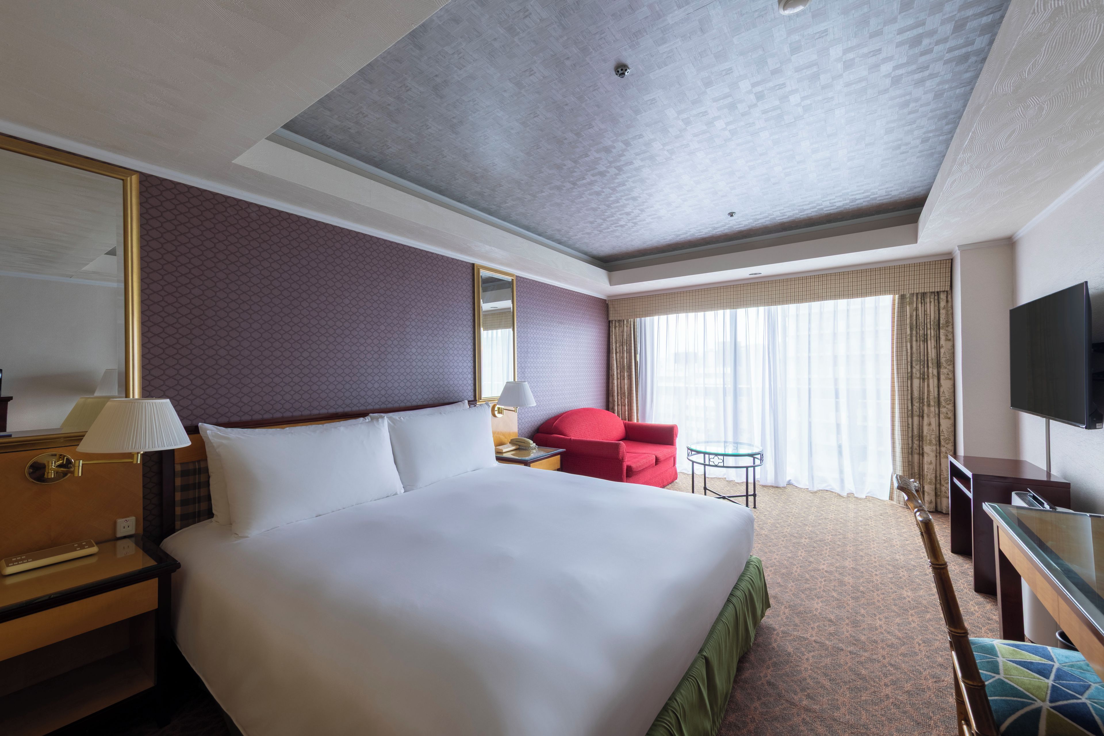 Une chambre d’hôtel avec un grand lit, un bureau, une télévision et une fenêtre avec des rideaux.