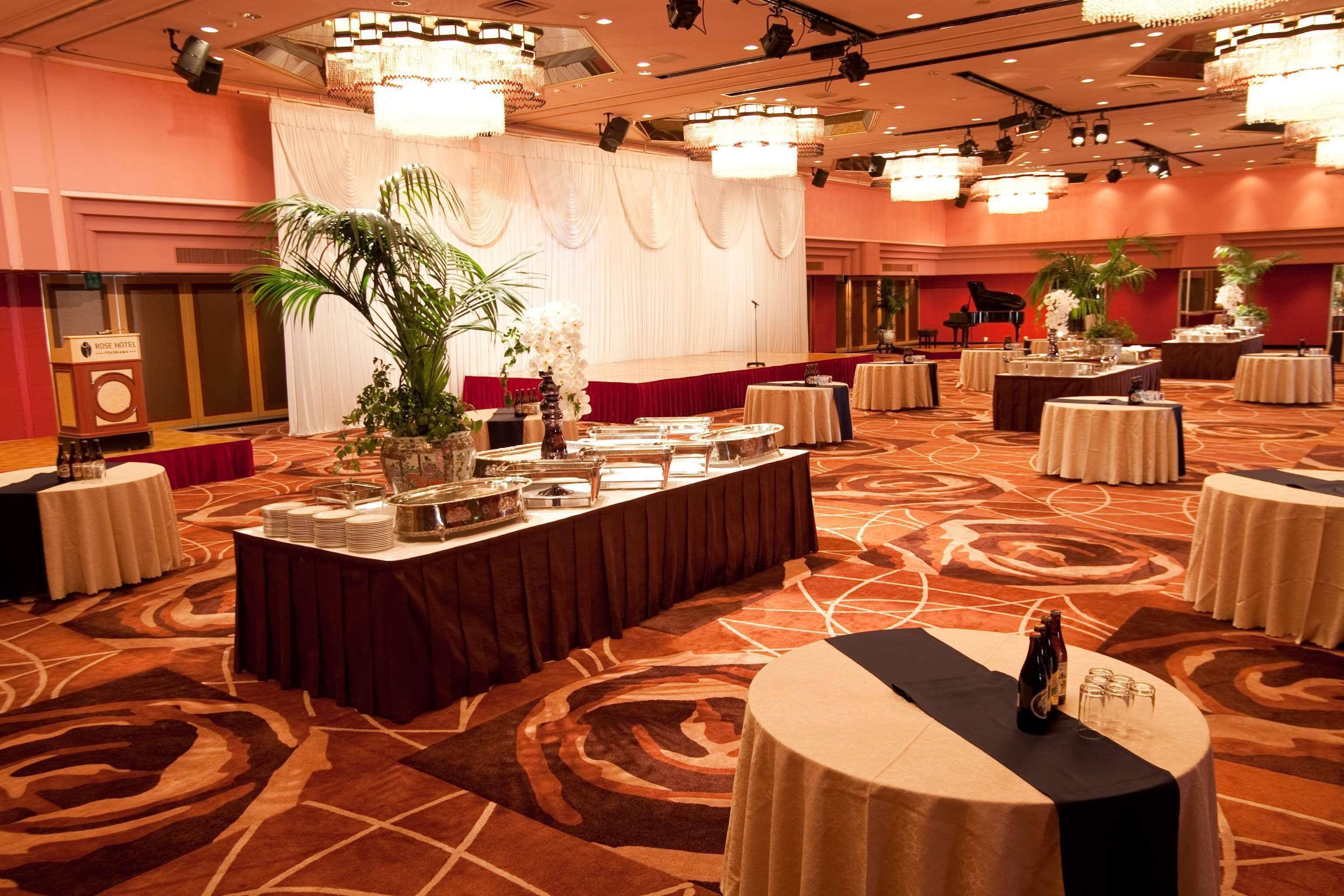 Un salón de banquetes con mesas redondas, un escenario y un piano.