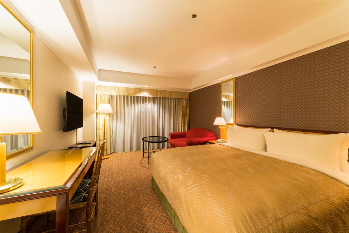 Habitació d'hotel amb un llit gran, escriptori amb làmpada, televisió i una cadira vermella.