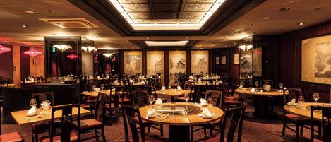 A restaurant with round tables, chairs, and a patterned carpet.
