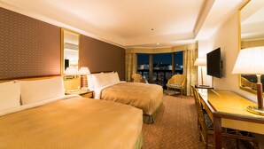 A hotel room with two beds, a desk, a chair, a TV, and a city view.