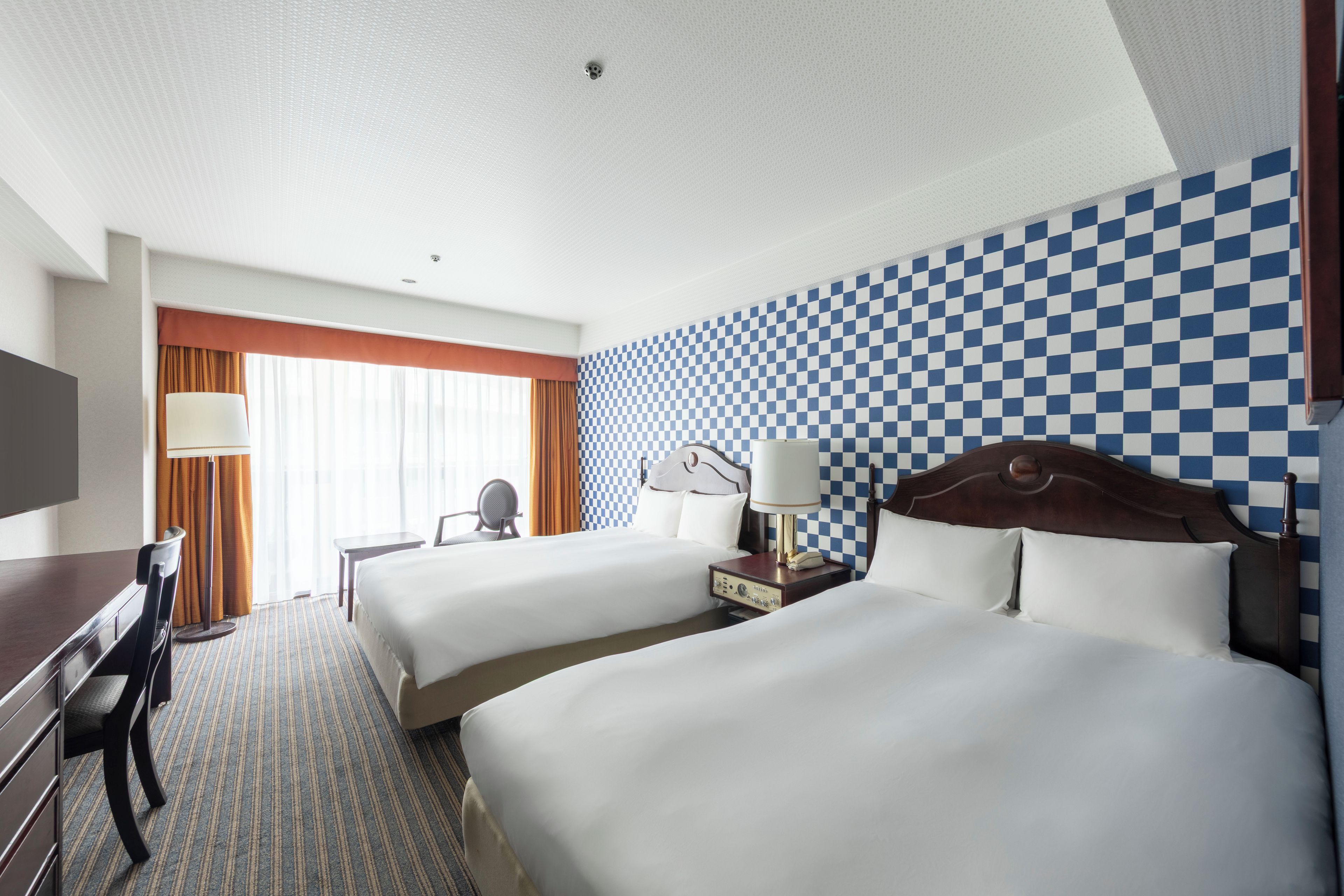 A hotel room with two beds, a desk, a chair, and a television.