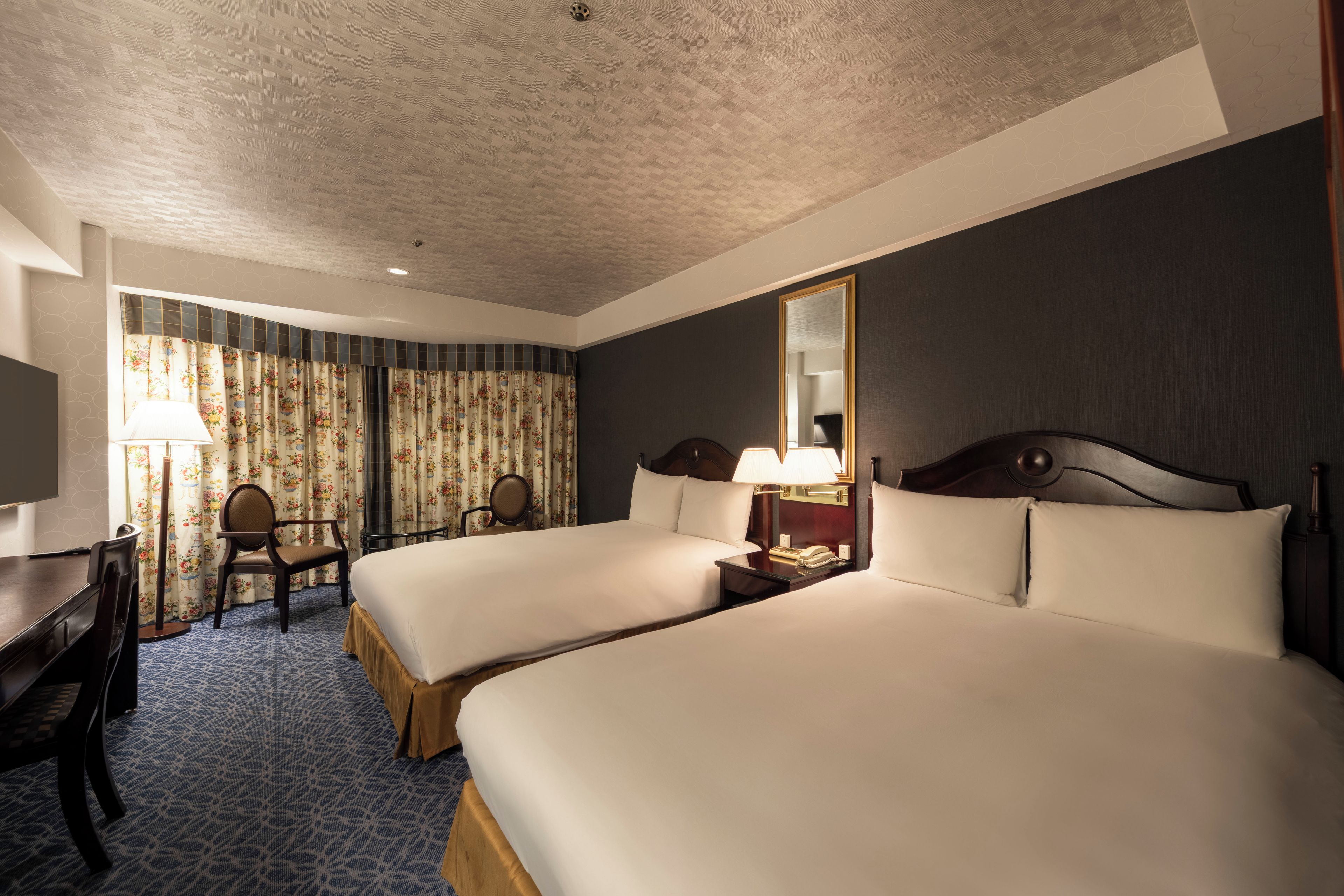Ein Hotelzimmer mit zwei Betten, einem Schreibtisch, einem Stuhl, einem Spiegel und einem Telefon.