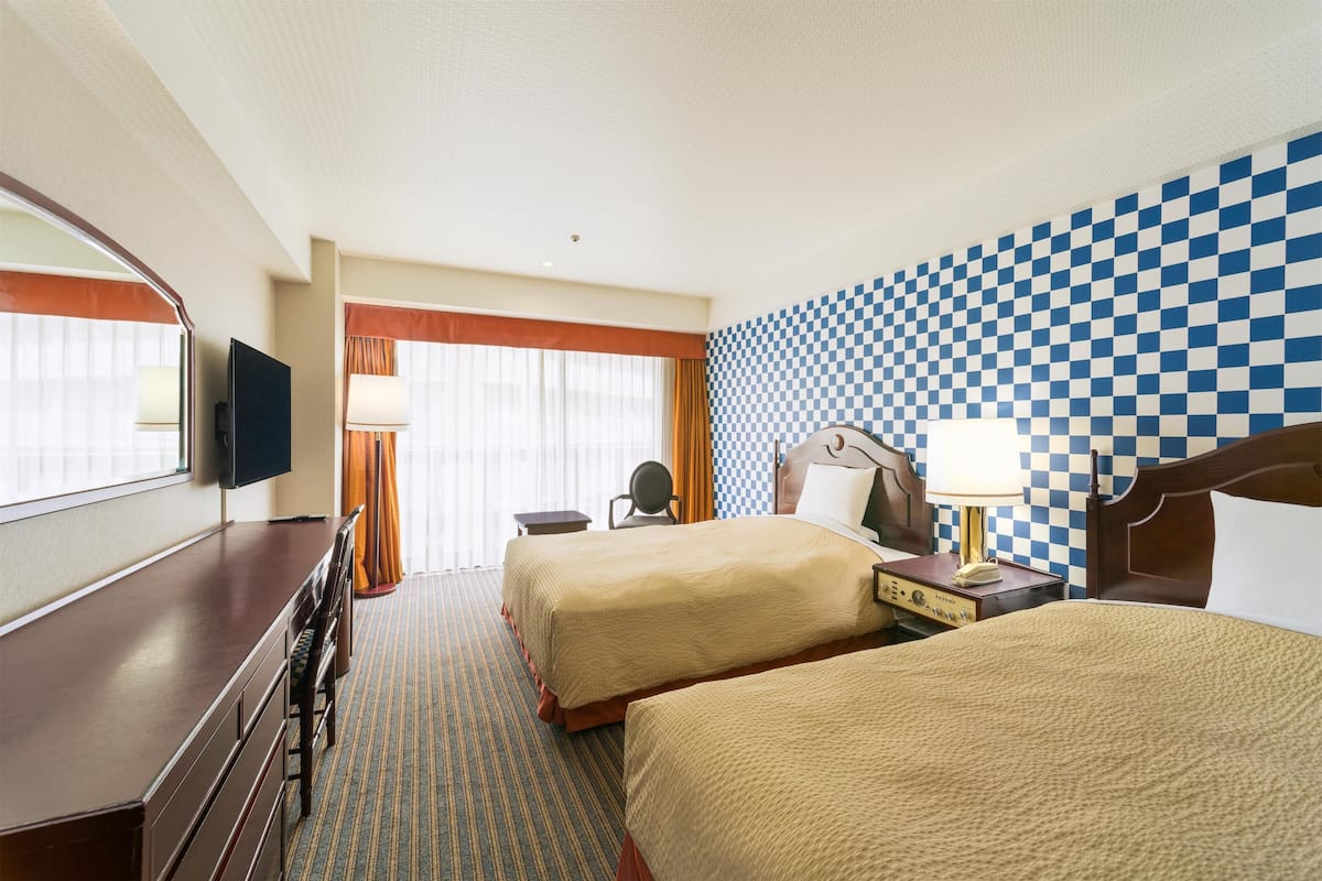 Habitació d'hotel amb dos llits, un escriptori, una cadira, una televisió i una paret amb quadres.