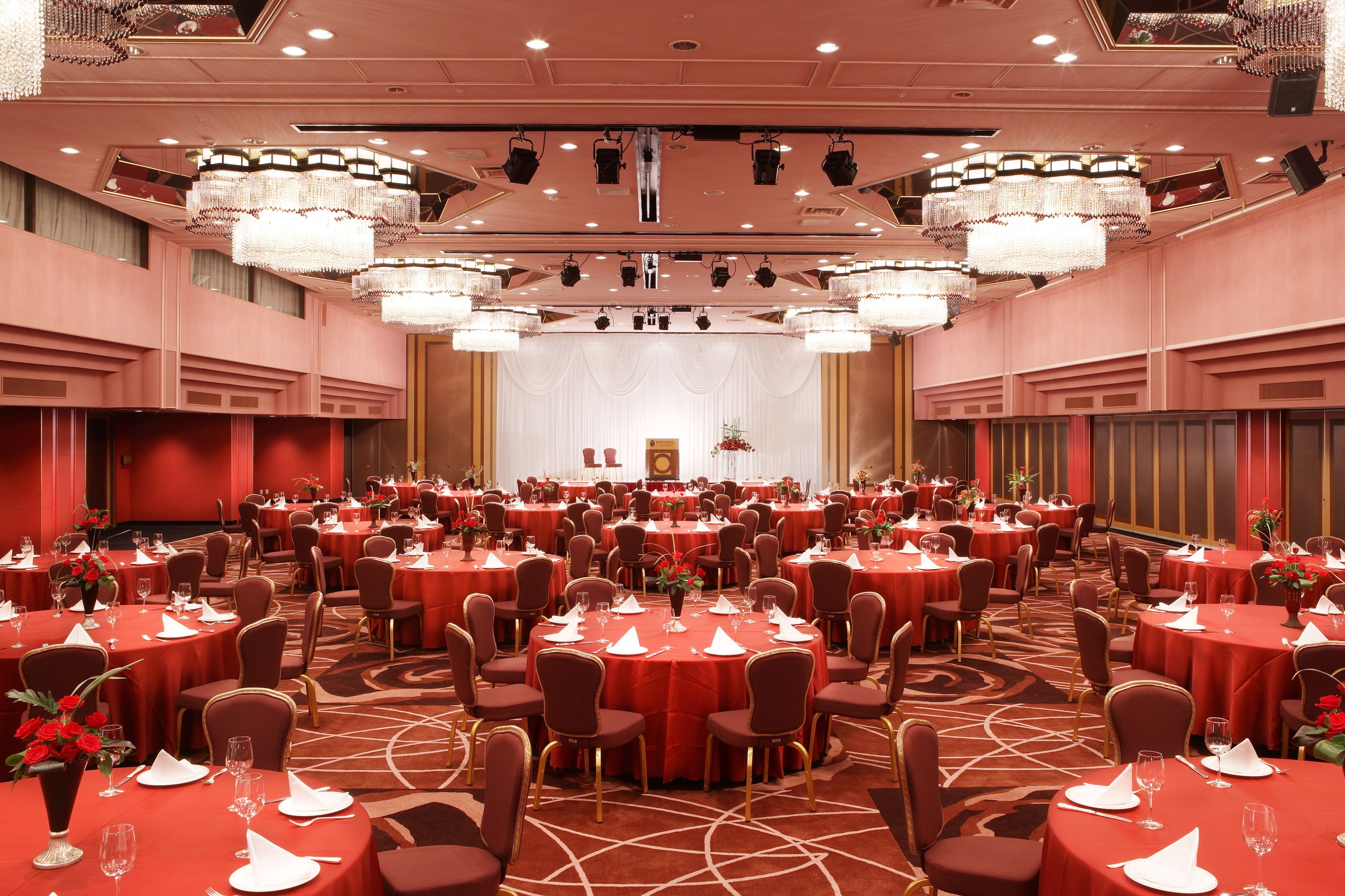 Une vaste salle de banquet avec des tables rondes, des nappes rouges et des chaises dorées.