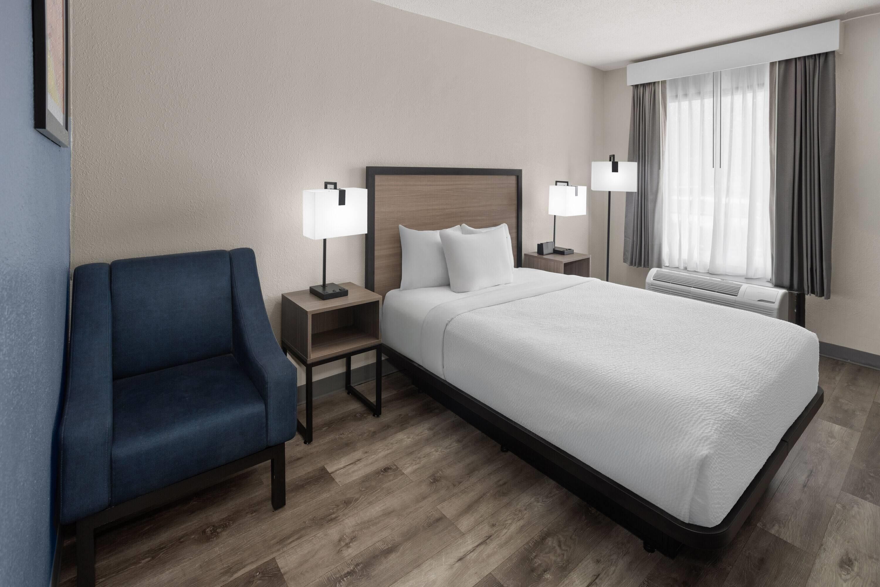 A hotel room with a bed, a chair, two bedside tables with lamps, and a window with curtains.
