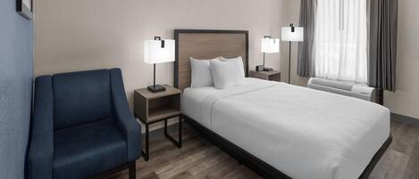 A hotel room with a bed, a chair, two bedside tables with lamps, and a window with curtains.