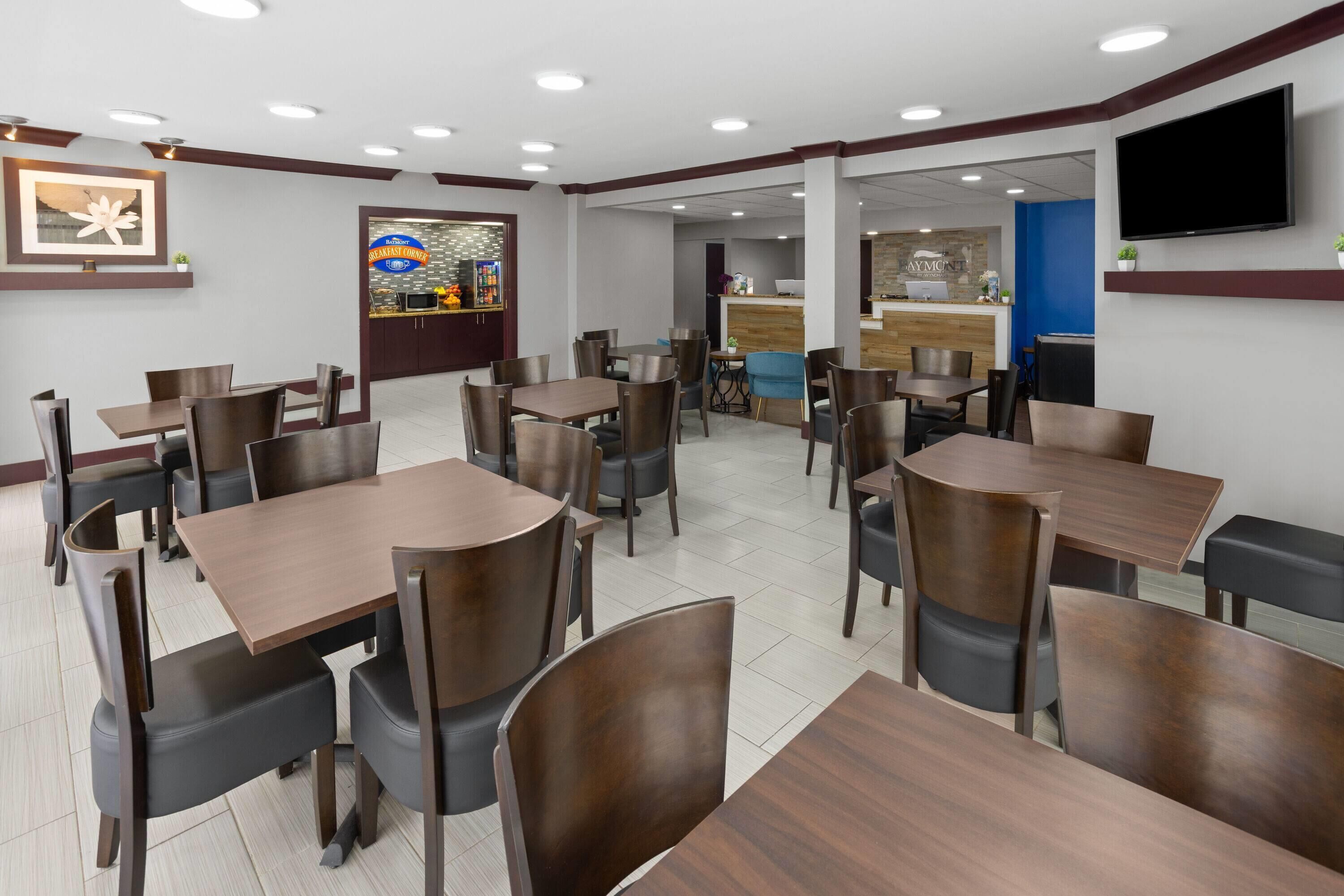 Un restaurante con varias mesas y sillas, una barra con menú, y un televisor en la pared.