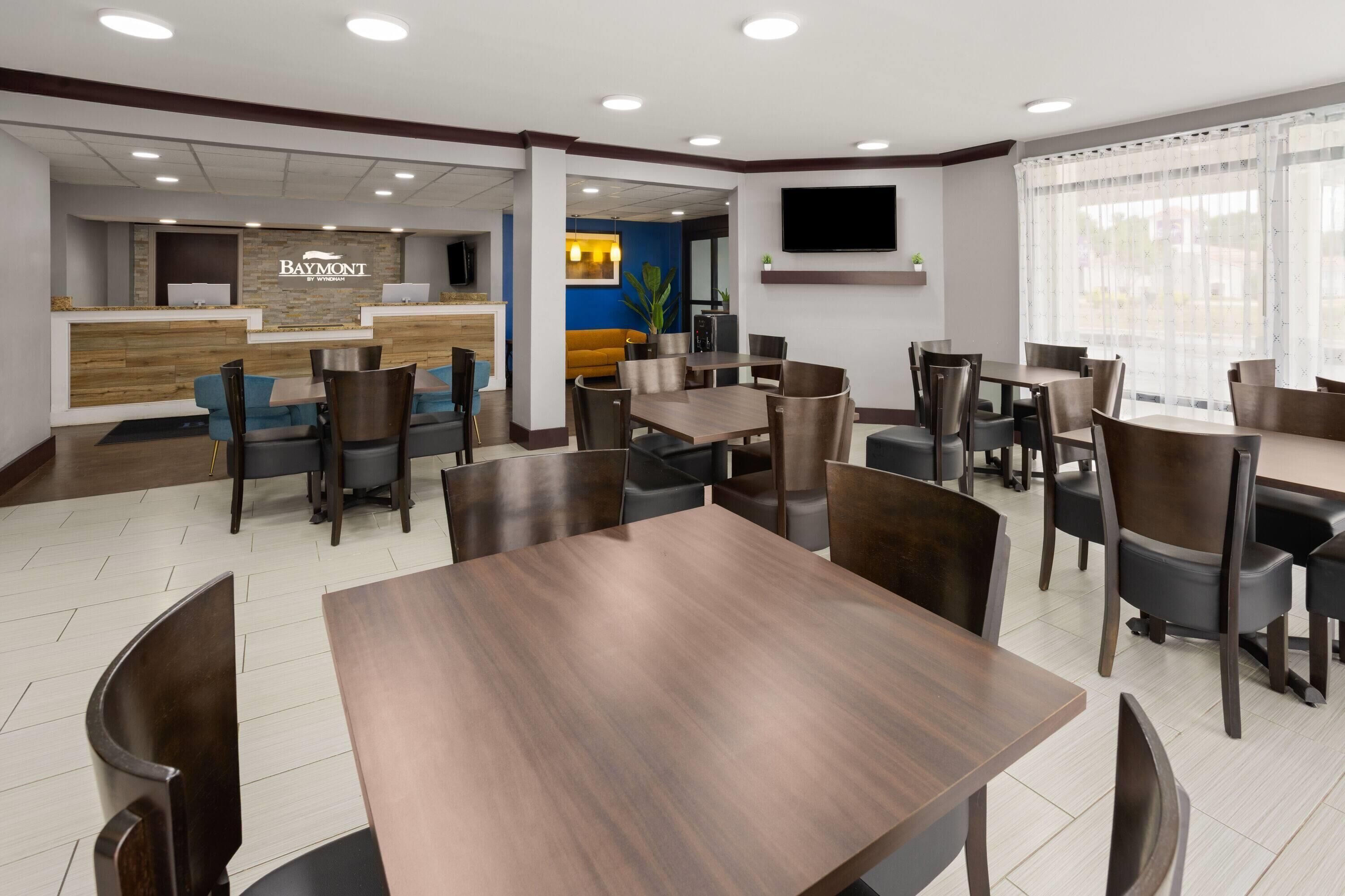 A restaurant with multiple tables and chairs, a reception desk, and a television screen.